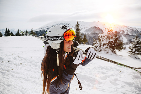 Leende tjej i skidbacke bärandes på ett par skidor