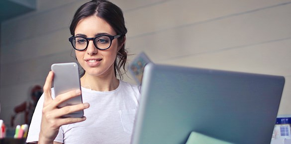 Kvinna i glasögon och brunt hår med dator och telefon