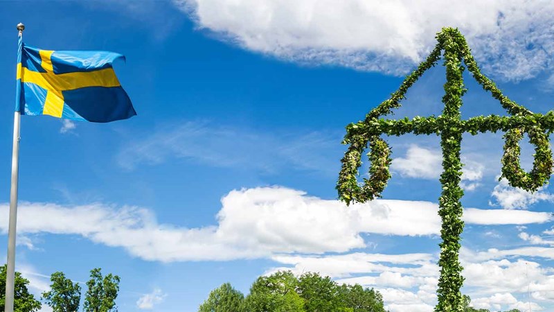 Flaggstång med svenska flaggan och en midsommarstång mot blå himmel