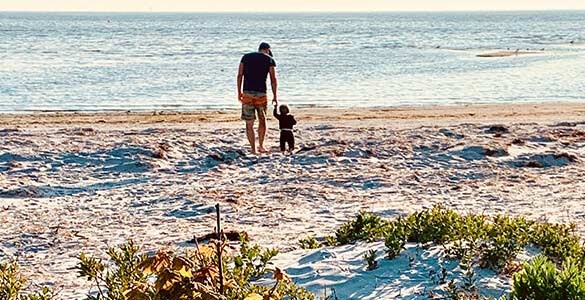 Far och son på sandstrand vid havet en sommarkväll