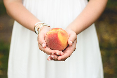 Kvinna med vit klänning som håller i en persika