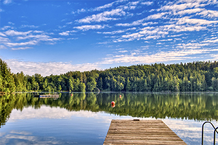 Sjö med brygga, skog och himmel