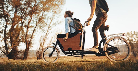 Man kör kvinna i lådcykel på en gräsmatta