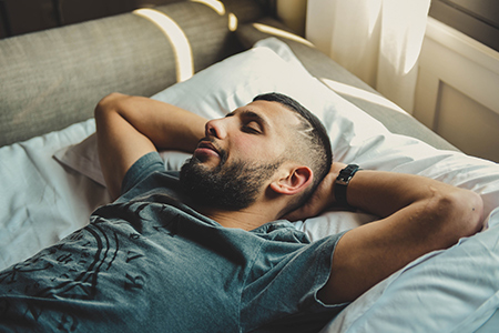 Man som ligger på en säng och sover med händerna bakom huvudet