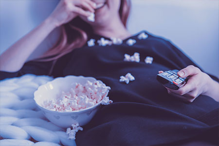 Kvinna som äter popcorn och håller en tv-kontroll i handen
