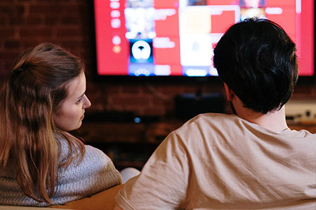 En kvinna och en man sitter i en soffa framför en tv och väljer film