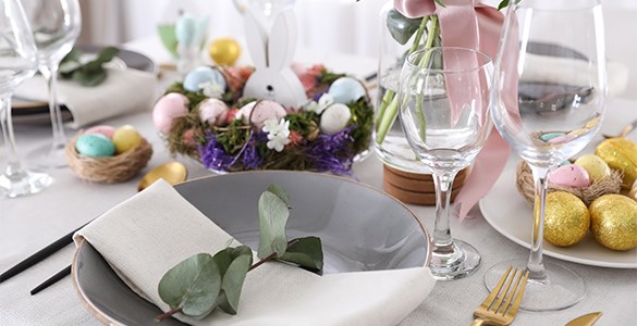 Påskdukat middagsbord med tallrikar, glas och dekorationer med målade ägg och blommor