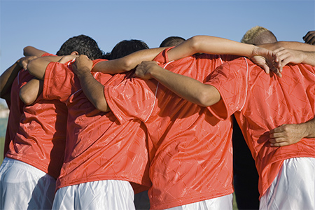 Killar med röda lagtröjor håller om varandra på fotbollsmatch 