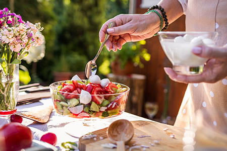 Kvinna med förkläde gör en sallad i utomhuskök