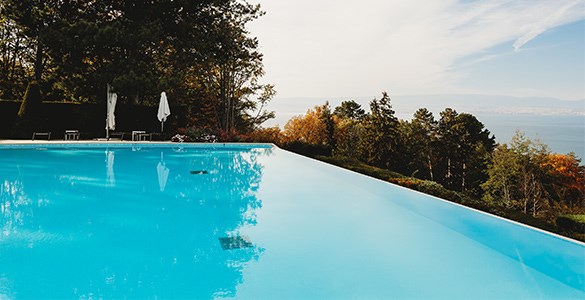 Stor swimmingpool med träd och hav i bakgrunden