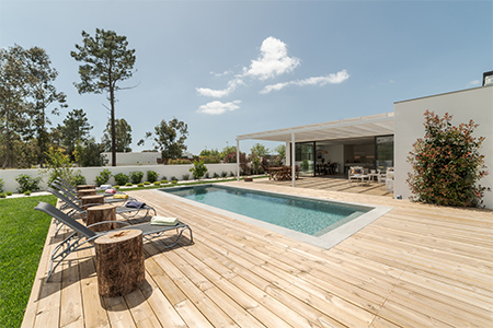 Pool på terrass med trädäck och solstolar vid villa