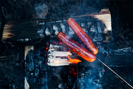 Grillkorv på grillspett över glödande kol i skogen