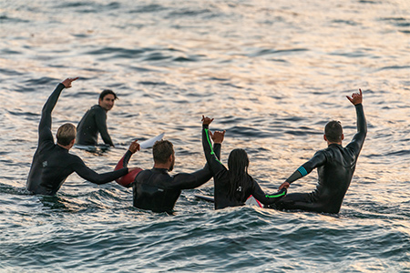 Fem surfare i vattnet som sträcker upp sina händer i luften