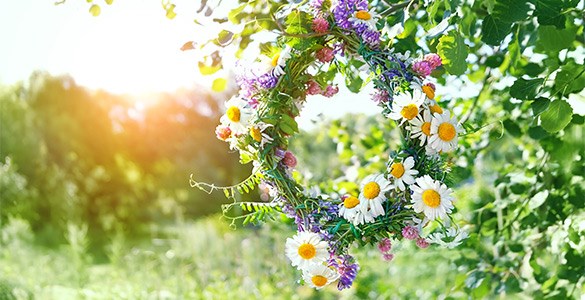 Midsommarkrans med svenska sommarblommor som hänger från ett träd på solig sommaräng