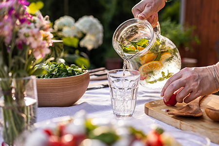 Person häller upp vatten smaksatt med örter och citron från karaff i glas utomhus