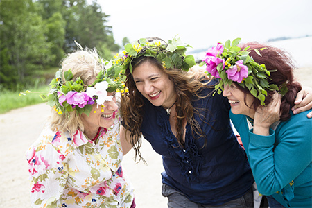 Tre skrattande kvinnor med blomsterkransar