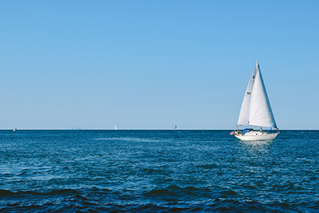 Segelbåt med vitt segel på havet med blå himmel en sommardag