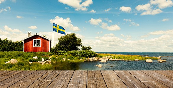 En liten röd stuga intill havet. Svenska flaggan är hissad framför huset. 