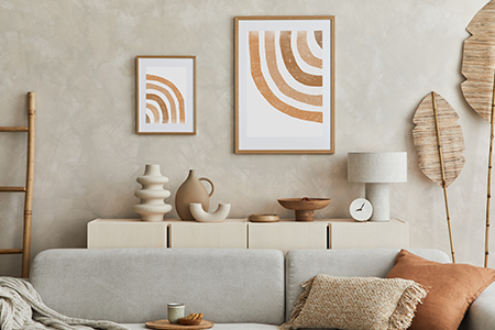 En sandfärgad vägg med abstrakta tavlor i roströda nyanser.