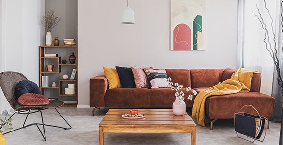 En roströd soffa med färgglada kuddar. Framför soffan står ett lågt soffbord i trä.