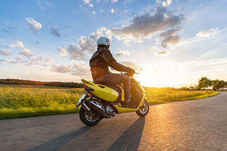 En moped kör längs en landsväg i solnedgången