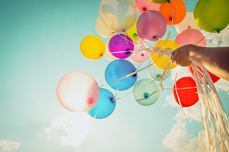 En hand håller en knippe färgglada ballonger med himlen i bakgrunden