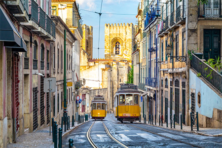 Två gula spårvagnar möts på en smal gata kantad av hus i Lissabon