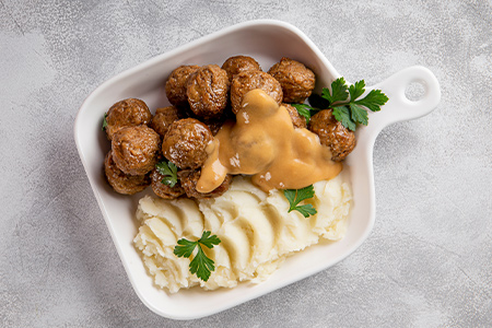 En portion köttbullar med potatismos och sås i en liten vit form