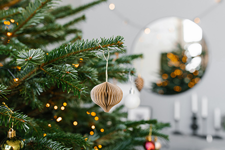 En gren i en julgran pyntad med en liten dekoration gjord av papper