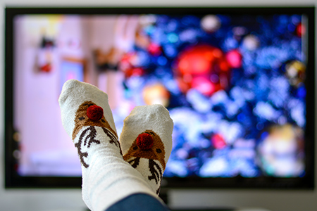 Ett par fötter i strumpor med juligt motiv framför en tv-skärm som visar en julfilm