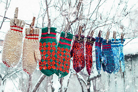 Fyra par hemmastickade vantar i olika mönster hänger på en tvättlina ute i snön