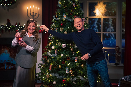 Lotta Engberg och Stefan Odelberg klär julgranen i en julpyntad Bingolotto-studio