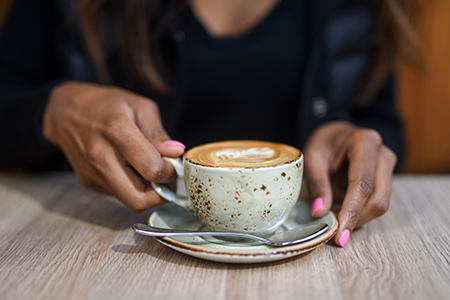 Ett par händer som håller i en mintfärgad kopp med kaffe i
