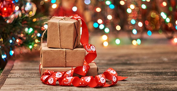 Två bruna paket står på varandra framför en julgran med färgglada ljus i