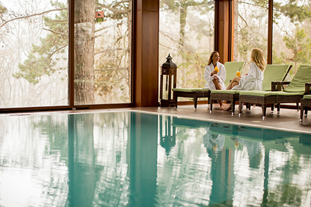 Två kvinnor i morgonrockar sitter vid kanten av en pool i ett spa