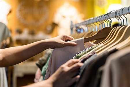 Ett par händer som går igenom kläder på en ställning i en second hand-butik