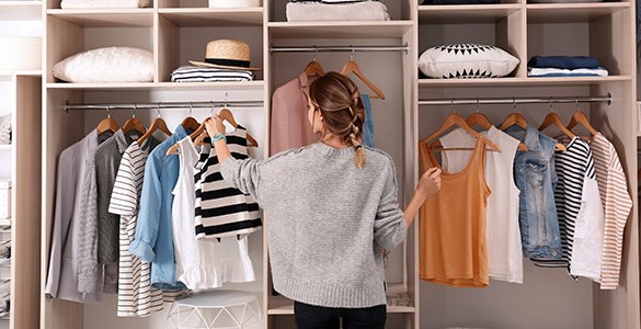 En kvinna står och väljer kläder i en prydligt organiserad garderob