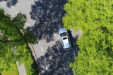 Foto ovanifrån på en bil som kör på en väg kantad av gröna träd