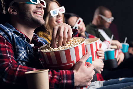 Ett par personer sitter i en biosalong. Äter popcorn och skrattar. 