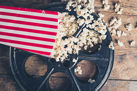 En gammeldags filmrulle ligger på golvet med en låda popcorn bredvid