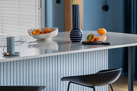En blå ribbad köksö med höga stolar framför. En stor vas och fruktfat står ovanpå köksön.