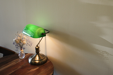 En liten lampa med grön skärm står på ett sidobord