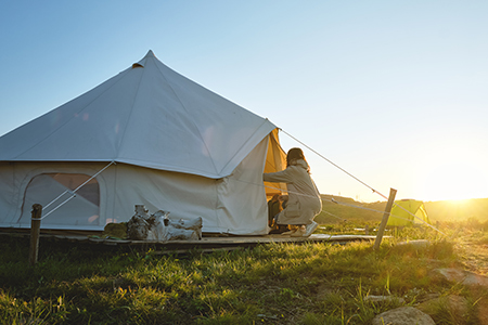 En kvinna är på väg in i ett glampingtält i soluppgången