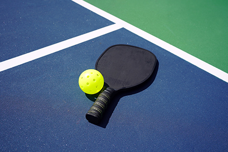 Ett svart pickleball racket och en neonfärgad boll ligger på marken