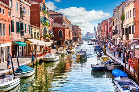 En kanal i Venedig kantad av förtöjda båtar och färgglada stenhus
